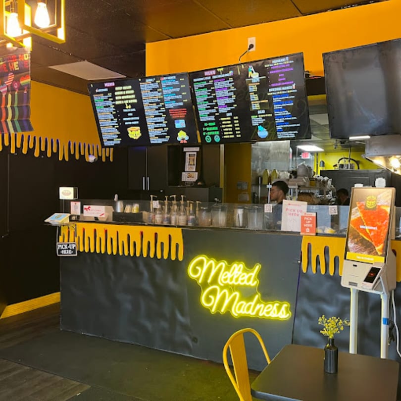 The Melted Madness restaurant interior with a neon sign, menu boards, and a counter.