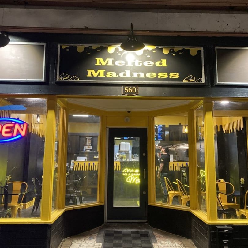 The Melted Madness restaurant exterior at night, with a black and yellow facade and an "OPEN" neon sign.